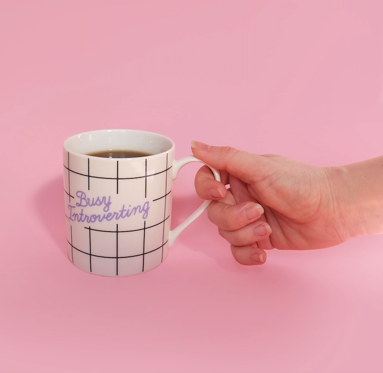 Hand hält Kaffeetasse mit der Aufschrift „busy introverting“