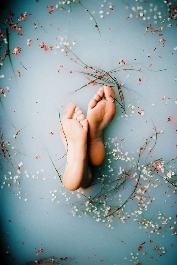 Füße schauen aus milchigem Badewasser mit Blüten heraus - ein Fußbad hilft bei dicken Beinen und Knöcheln.