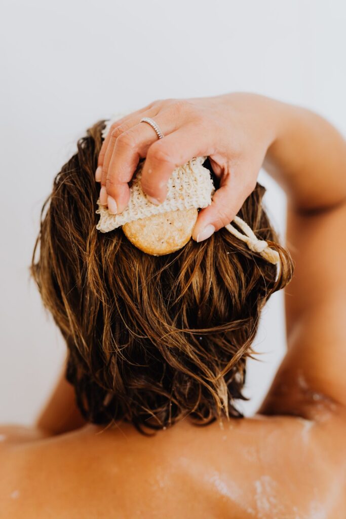 Eine Frau benässt mit einem Kopfhautschwamm ihre Haare, vielleicht um die fettigen Haare zu waschen.