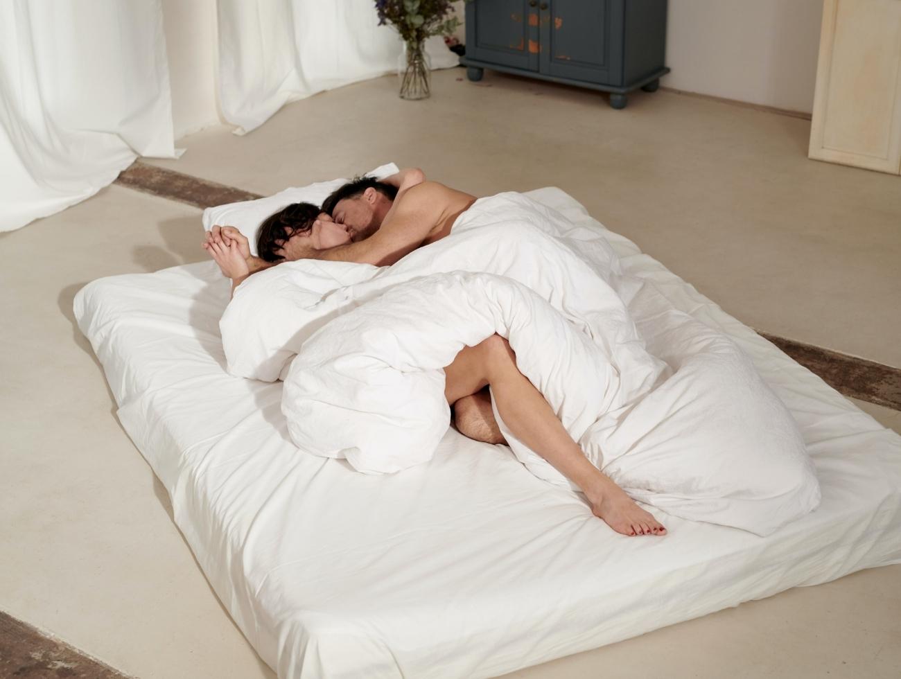 Ein Paar liegt nackt auf einer Matratze.