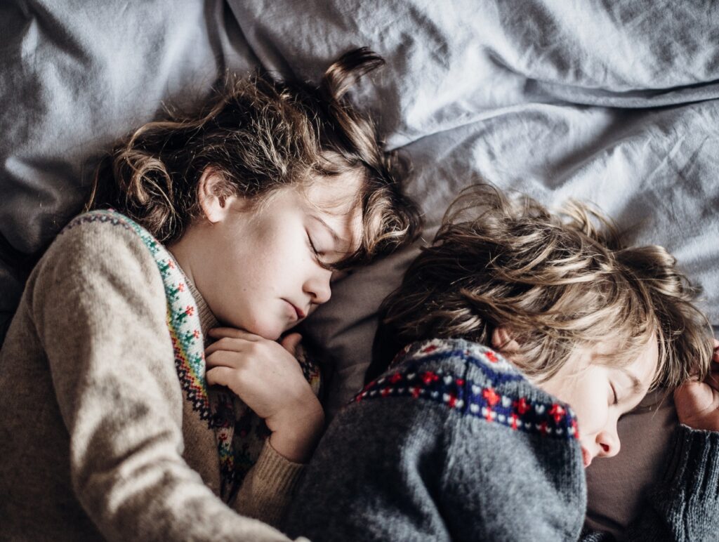 Geschwister schlafen nebeneinander zusammengekuschelt im Bett
