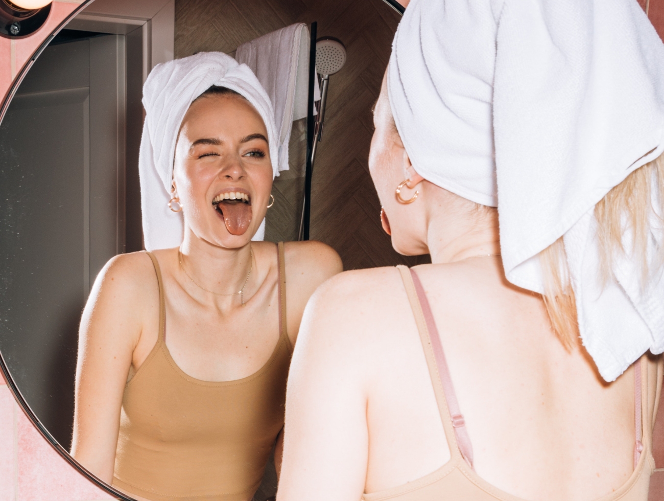 Eine junge blonde Frau zeigt ihrem Spiegelbild im Badezimmer die Zunge.