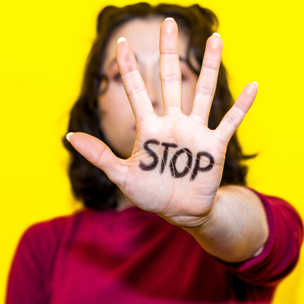 junge Frau vor gelbem Hintergrund streckt Hand mit dem Schriftzug "Stop" aus, macht gegen Gewalt aufmerksam.