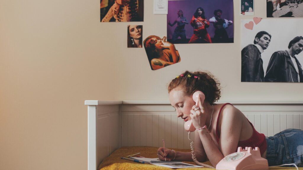 Junge Frau telefoniert mit einem Telefon, im Hintergrund hängen Poster