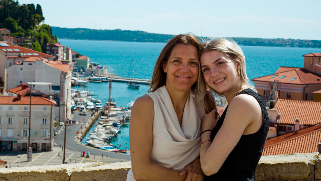 Mutter Isabel und Tochter Livia lächeln, im Hintergrund sieht man das Stadtbild Piran