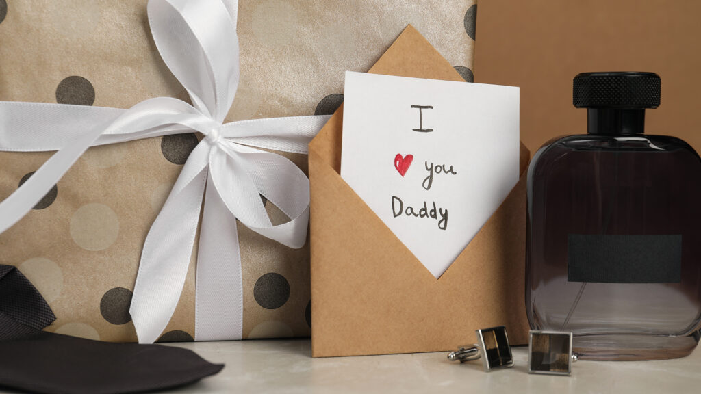 Happy Father's Day. Card with phrase I Love You, Daddy in envelope, cufflinks, perfume and gift box on light marble table, closeup