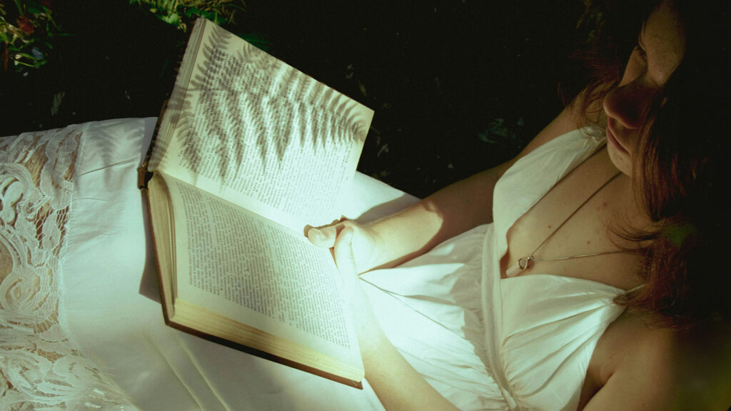Bücher: Bild von oben von einer jungen Frau im weißen Sommerkleid, die ein geöffnetes Buch in den Händen hält.
