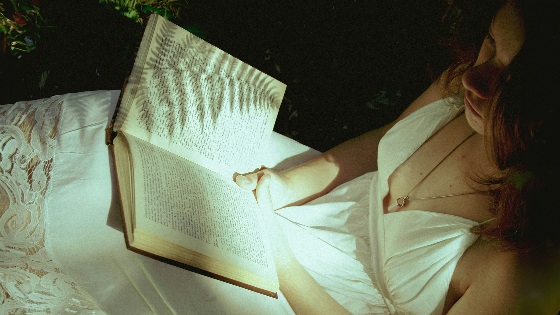 Bücher: Bild von oben von einer jungen Frau im weißen Sommerkleid, die ein geöffnetes Buch in den Händen hält.