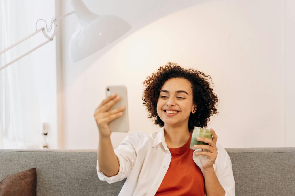 Ein Mädchen lächelt in ihr Smartphone, in der rechten Hand hält sie einen grünen Smoothie