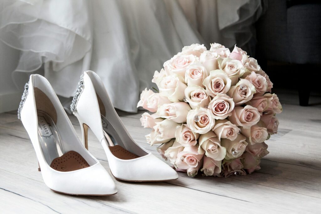 Weiße Schuhe und ein Hochzeitsstrauß mit hellrosa Rosen