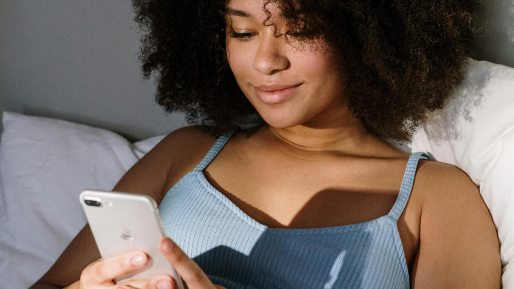 Frau liegt im Bett und schaut aufs Smartphone, Cortisol senken