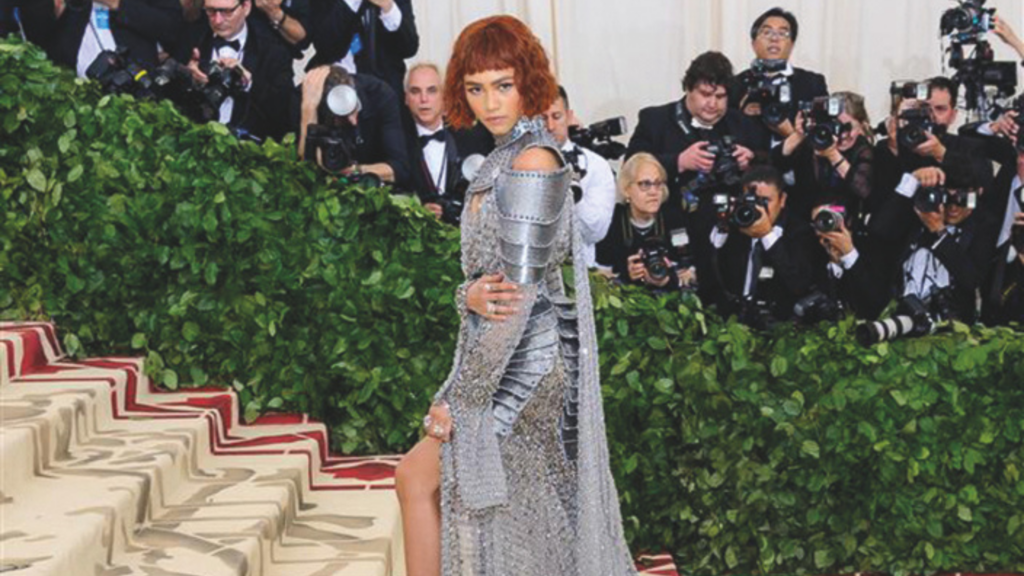 Zendaya in einem silber Kleid an eine Ritterrüstung angelehnt