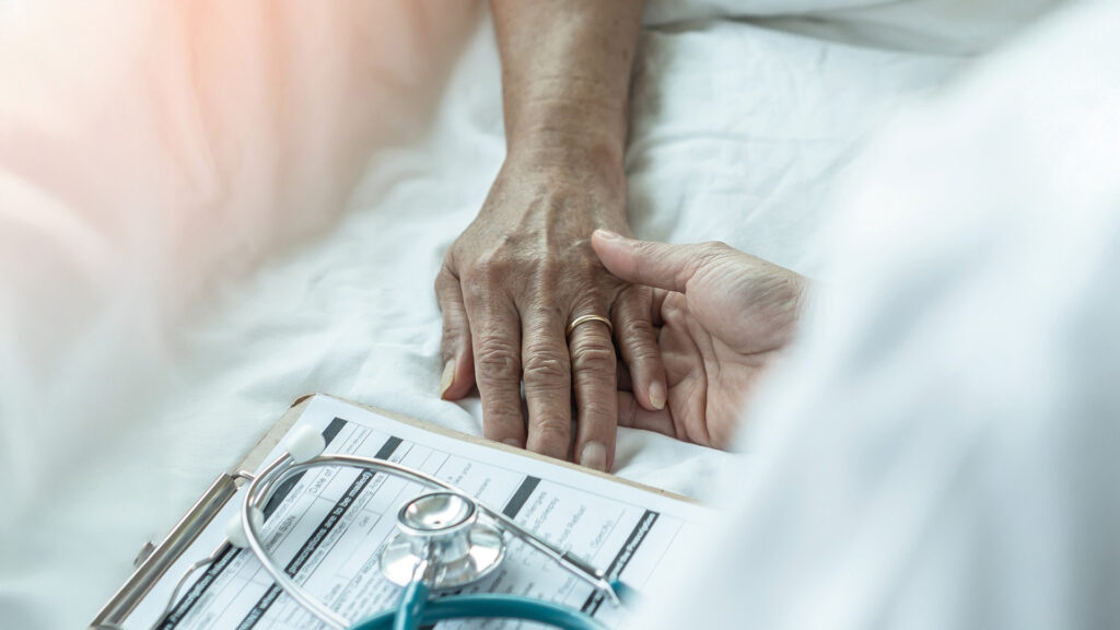 Arzt oder Pfleger hält fürsorglich die Hand einer älteren Person im Krankenhausbett