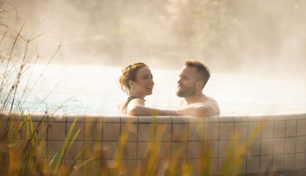 Ausflugsziele Steiermark: Ein junges Pärchen genießt Zweisamkeit in einem sonnigen Thermalbecken im Freien.