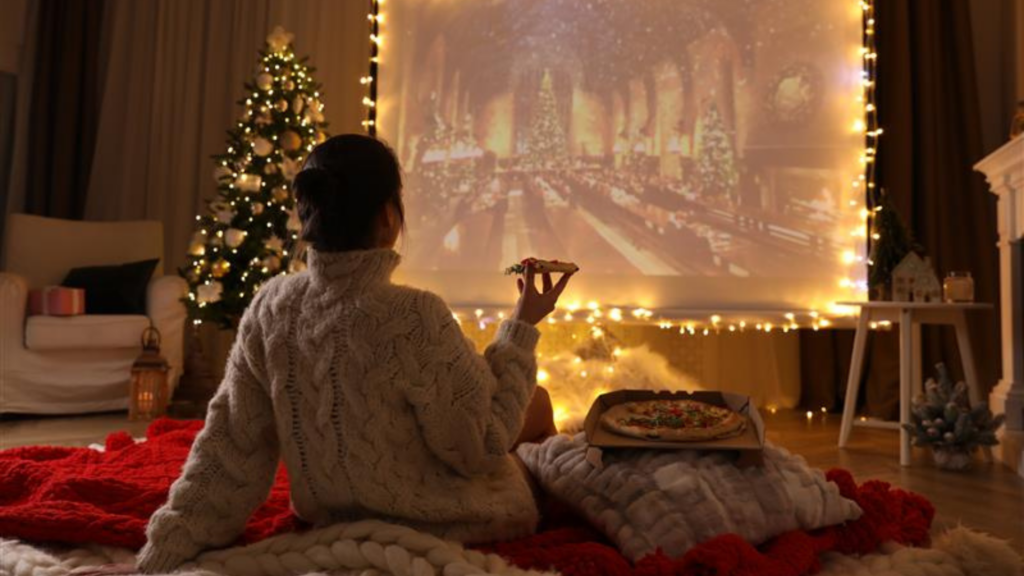 Frau sitzt mit Pizza vor einer Leinwand, auf der ein Weihnachtsfilm läuft