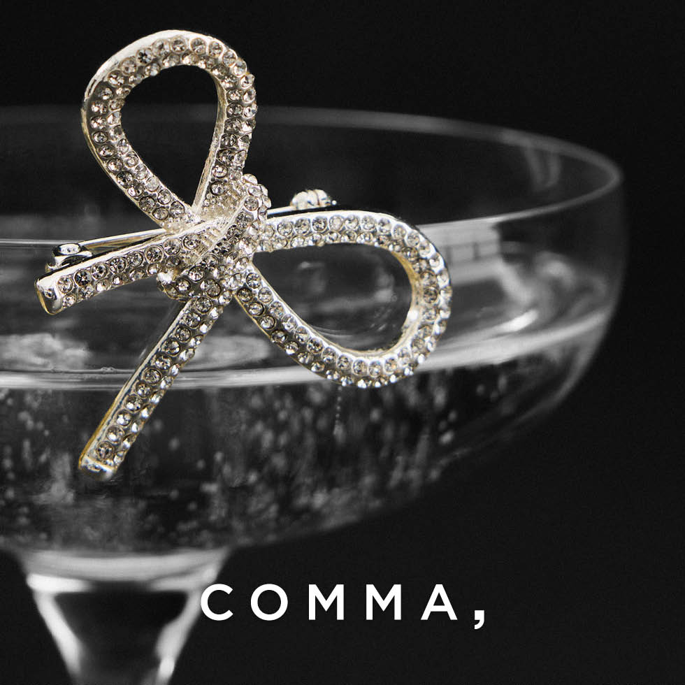 Adventkalender 2025 Tür 19: Comma Gutschein, eine Comma Brosche verziert ein Glas