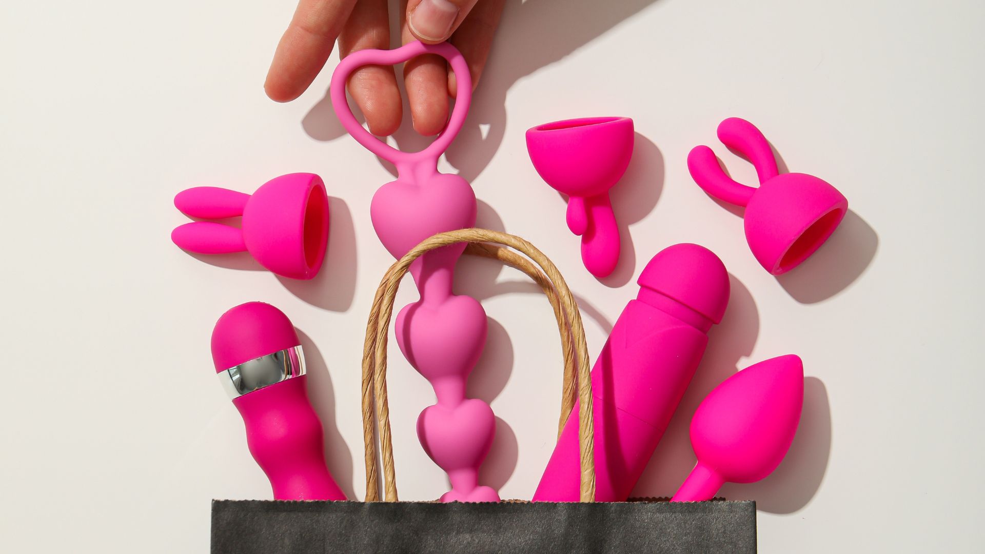 Hand zieht bunte Sextoys aus einer Tasche