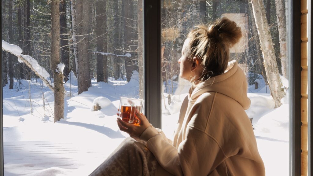 Frau sitzt vor Fenster und schaut in die schneebedeckte Natur