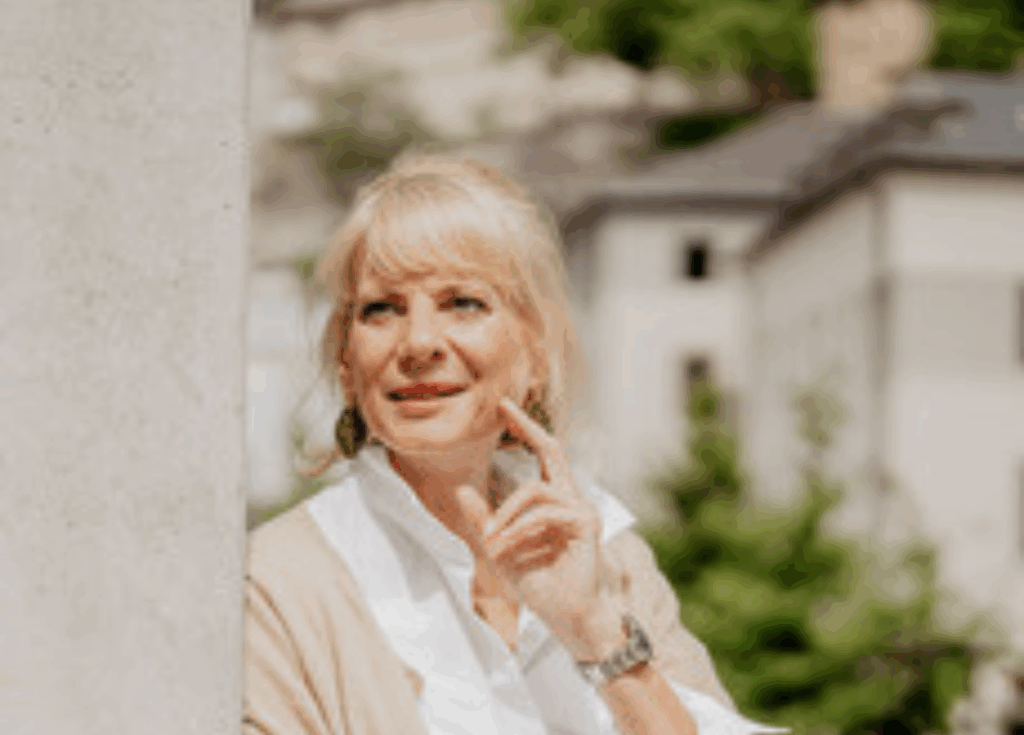 Dr. Sabine Viktoria Schneider im Portraitbild, sie lehnt an eine Wand mit der linken Hand im Gesicht als Pose