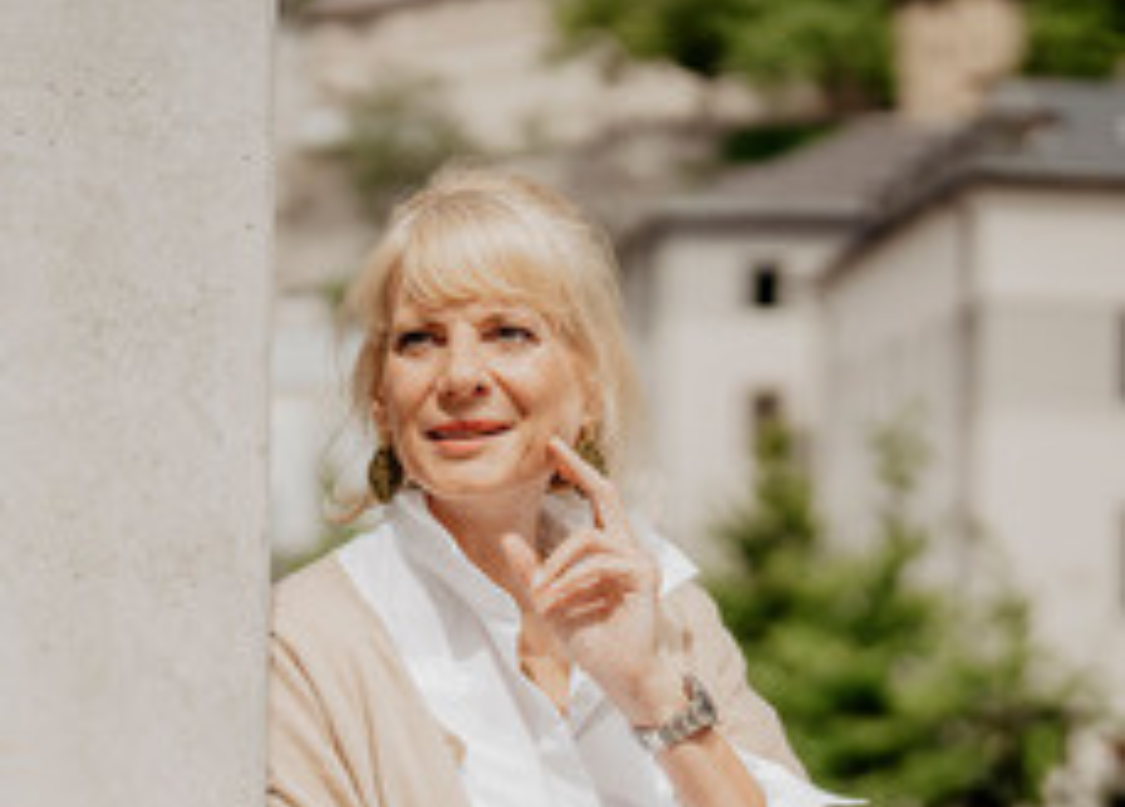 Dr. Sabine Viktoria Schneider im Portraitbild, sie lehnt an eine Wand mit der linken Hand im Gesicht als Pose