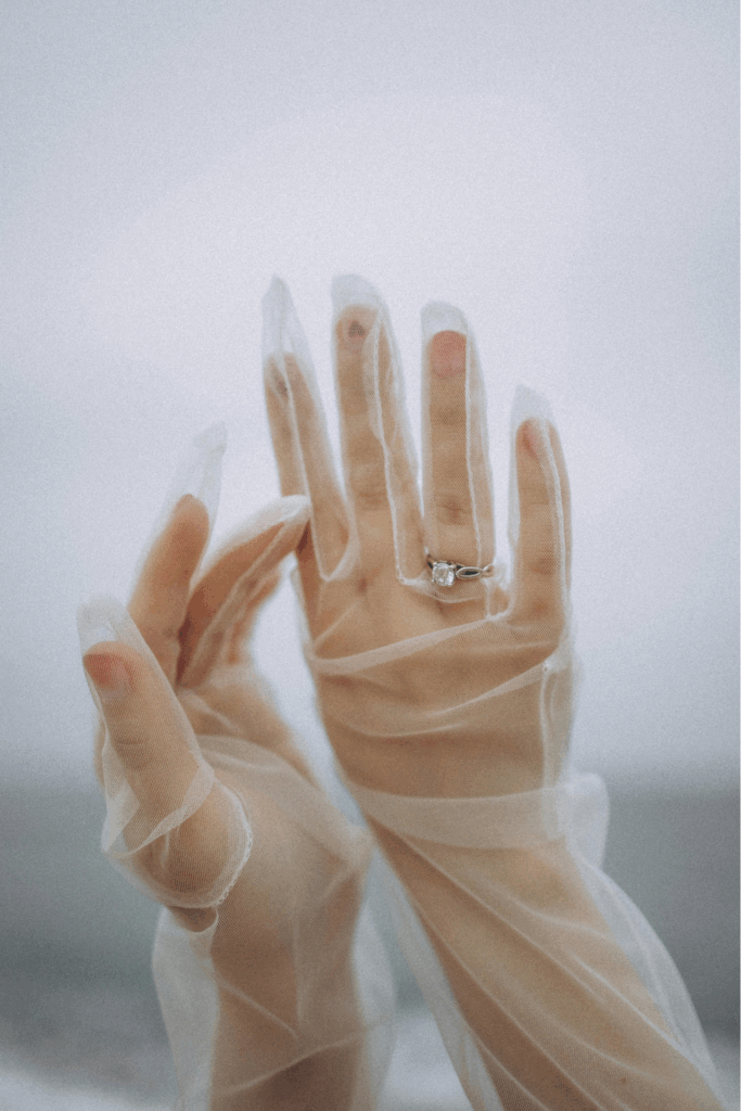 Zwei Frauenhände in durchsichtigen Handschuhen mit einem Verlobunsgring.