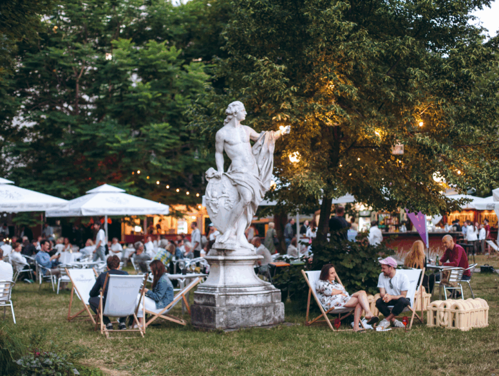 Garten des Palais Auersperg mit Liegestühlen, Lichterketten, einer Statue in der Mitte und sitzenden Menschen