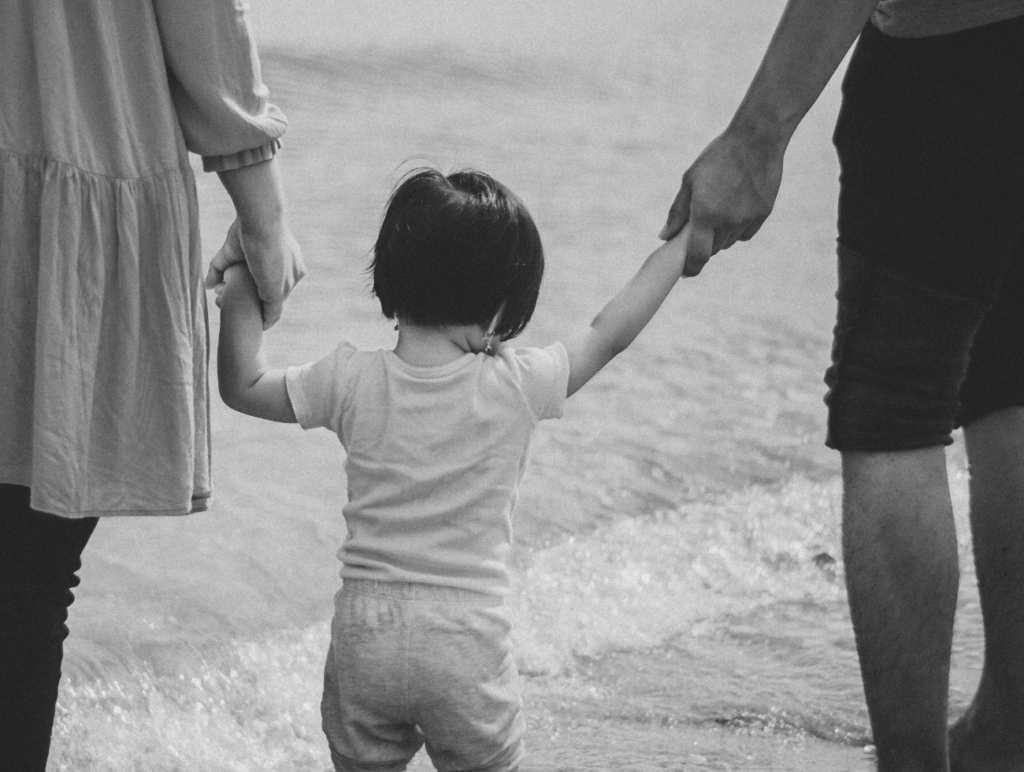 Ein Kind wird links und rechts an der Hand gehalten und geht einen Strand entlang