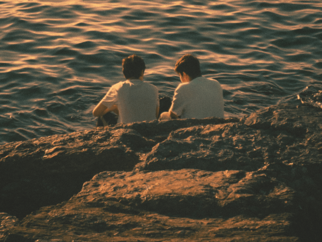 Zwei Männer sitzen auf einem Felsen und schauen ans Meer