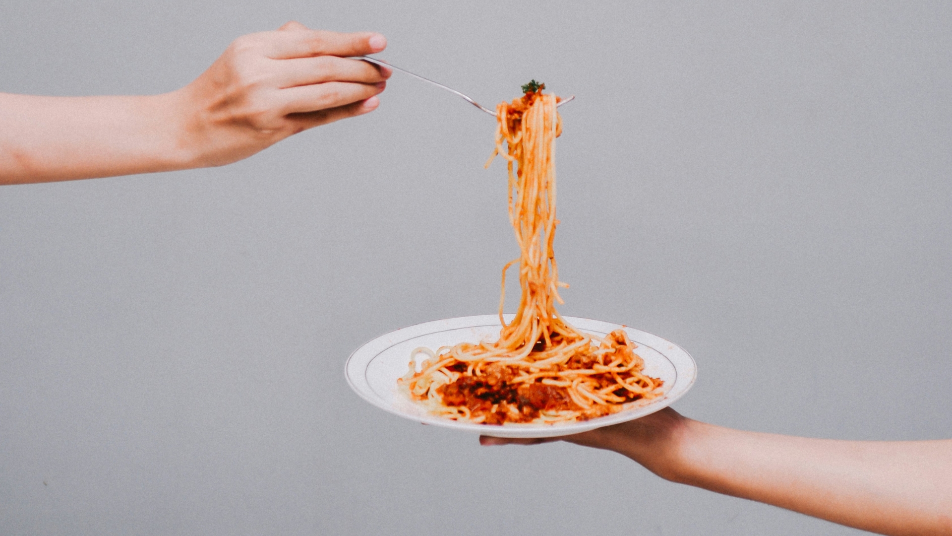 Teller Pasta wird mit einer Hand gehalten, andere Hand wickelt Spaghetti auf Gabel auf